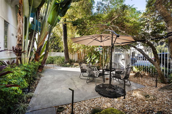 Outdoor patio area with a table, chairs, and umbrella surrounded by greenery.
