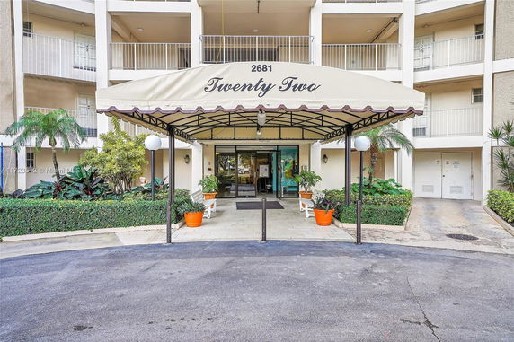 Front view of a multi-story building entrance with a covered awning and plants.