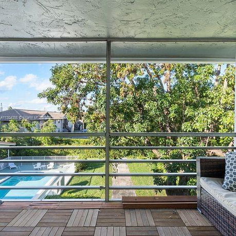 Balcony view overlooking a swimming pool and trees with railing and outdoor seating.