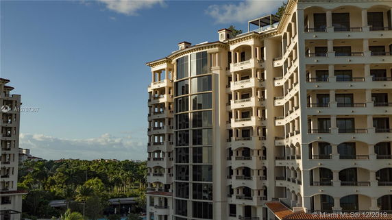 Multi-story building with balconies and large central windows, surrounded by greenery.
