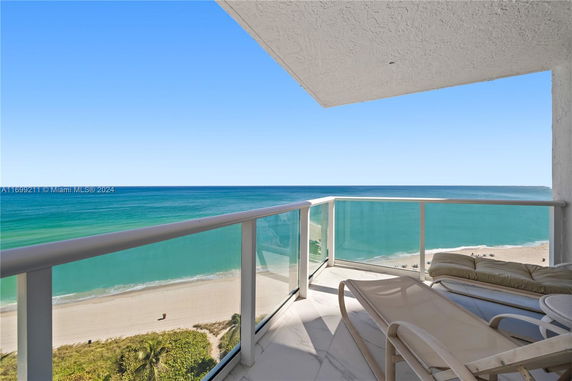 Balcony view overlooking the ocean with clear glass railings and lounge chairs.