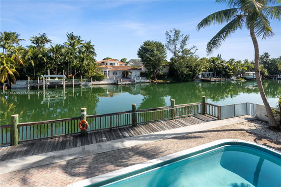 Outdoor area with a swimming pool and a view of a waterfront with houses and trees on the opposite side.