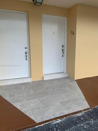 Front view of a yellow building with two white doors and tiled doorstep.