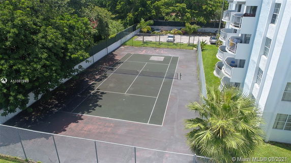 View of an outdoor tennis court next to a multi-story building.
