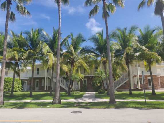 Front view of a two-story building with multiple staircases and surrounded by palm trees.