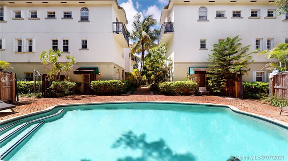 View of a swimming pool between two buildings with multiple windows and balconies.
