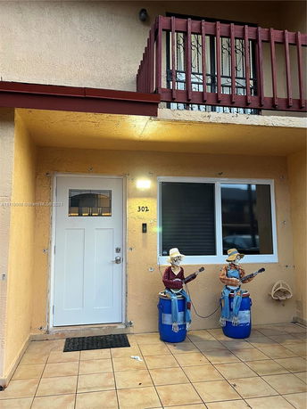 Front view of a multi-story building entrance with a balcony and two decorative skeleton figures by the door.