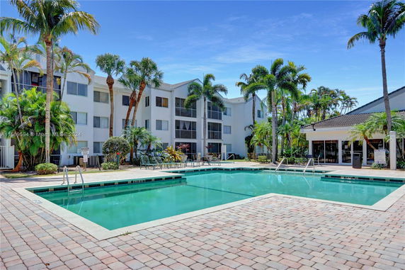 Outdoor swimming pool area in front of a multi-story residential building.
