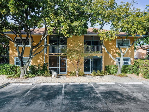 Front view of a two-story building with balconies and surrounding trees.