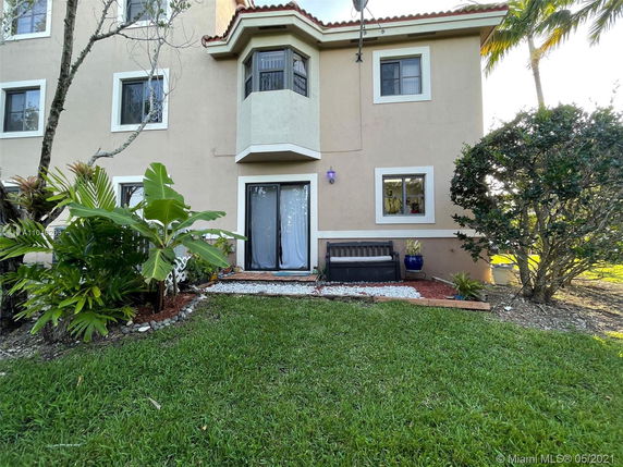 Front view of a multi-story house with a bay window and decorative plants in the yard.