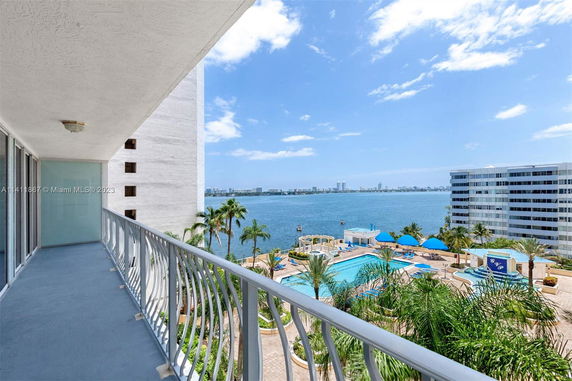 Balcony view overlooking a body of water with surrounding buildings and pool area.