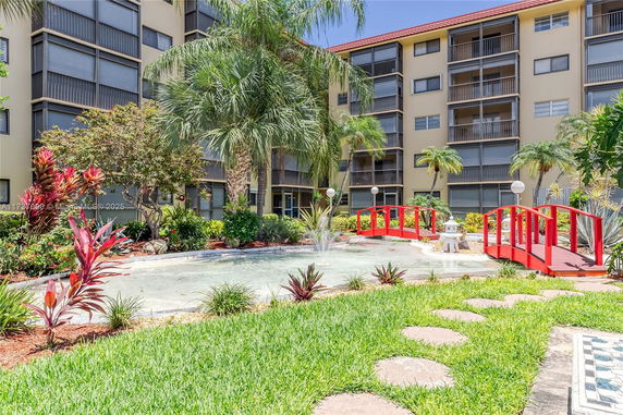 Multistory residential building with balconies and a garden featuring a pond and red bridges.