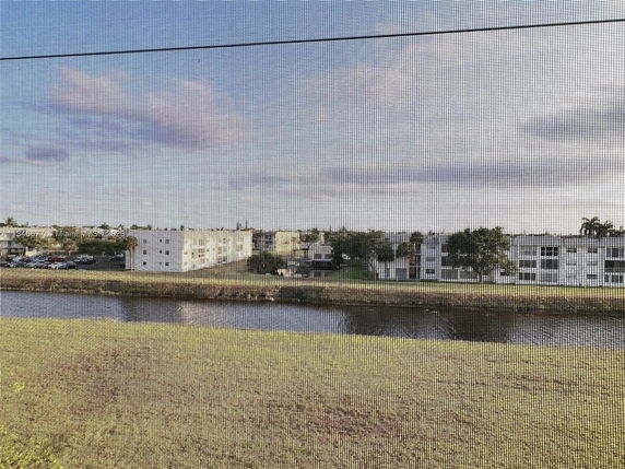 View of apartment buildings across a waterway with grassy area in the foreground and a cloudy sky.