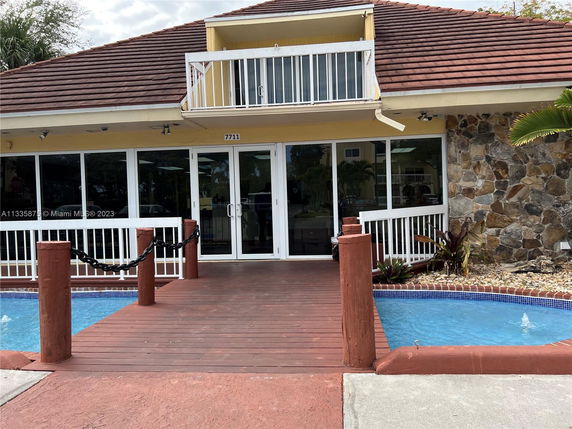 Front view of a building with a balcony and a walkway over a small pool.