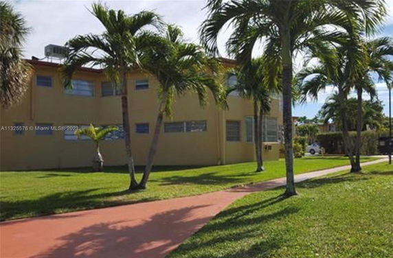 Front view of a two-story building with several windows and surrounded by palm trees.