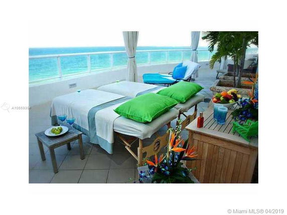 Outdoor balcony setup with massage tables, green pillows, and ocean view.