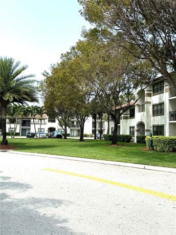 Front view of a multi-story apartment building with balconies and a landscaped area with trees.