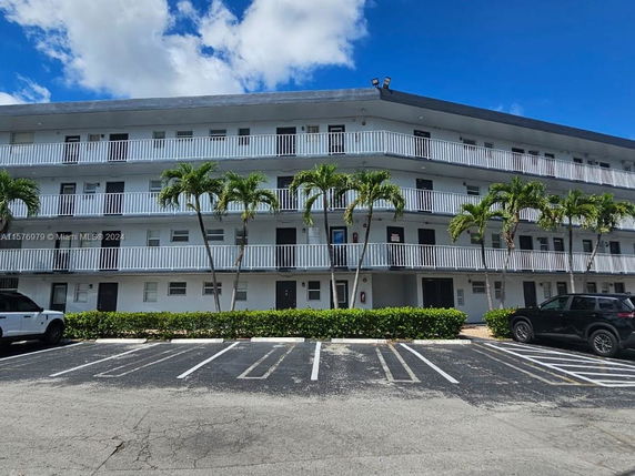 Front view of a multi-story building with balconies and palm trees.