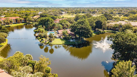Aerial view of a landscaped residential area with a central lake and fountain, surrounded by multiple houses and lush greenery.
