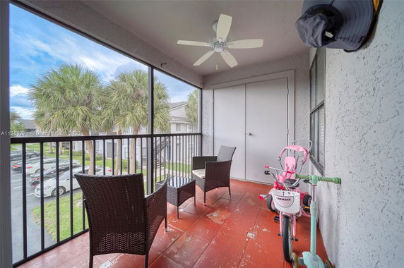 Balcony view with chairs, ceiling fan, and palm trees visible in the background.