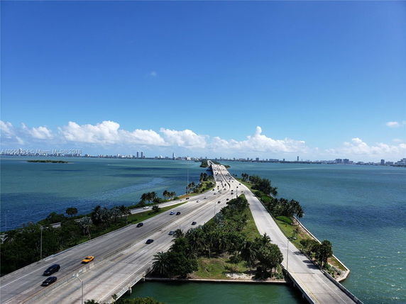 Wide view of a road leading across a body of water with a cityscape in the distance.