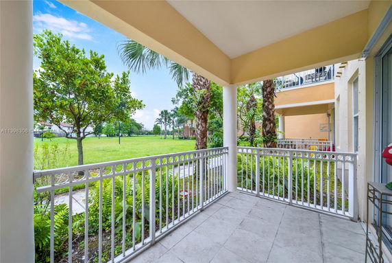 View from a covered patio overlooking a grassy area with trees and other buildings.