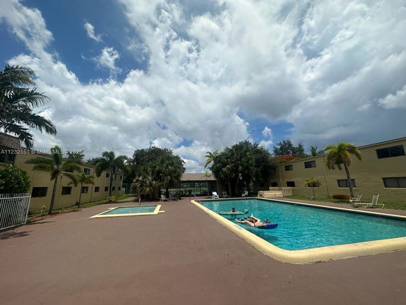 Outdoor view of swimming pool area with surrounding buildings and palm trees.