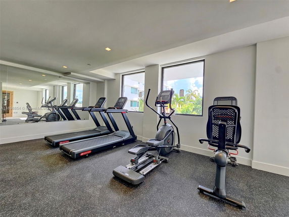 Indoor gym area with exercise equipment including treadmills and a stationary bike, featuring a large mirror wall and windows.