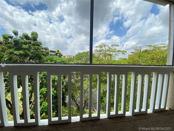 Balcony view overlooking trees and partially cloudy sky