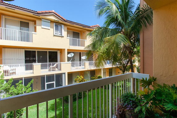 View from a balcony overlooking a courtyard in a residential building with palm trees and grass.