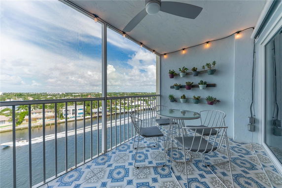 View from a balcony with a glass table and chairs, overlooking a waterway and distant houses.