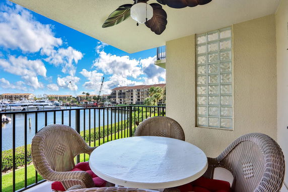Outdoor balcony with a table and wicker chairs overlooking a marina.