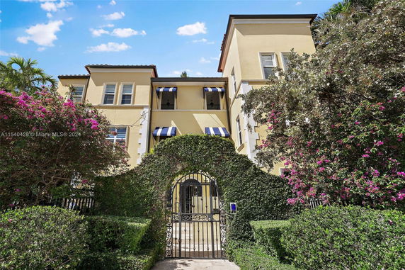 Front view of a multi-story house with yellow walls and blue striped awnings.