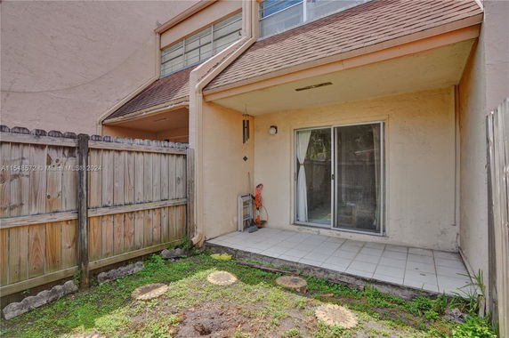 View of a small patio area with sliding glass doors and wooden fence.