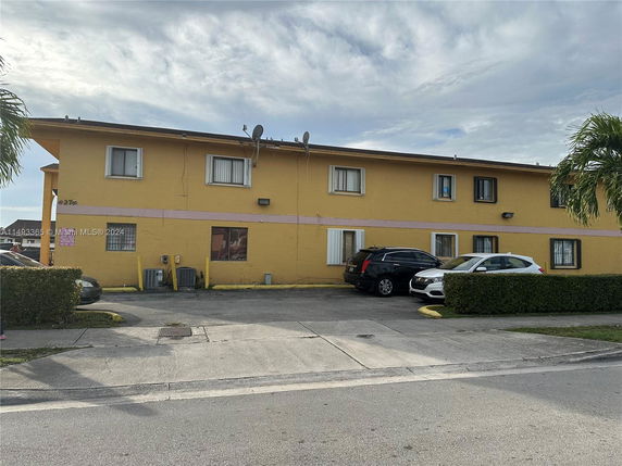 Front view of a two-story building with yellow exterior and parking area.
