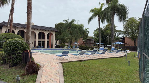 Outdoor swimming pool area with lounge chairs and surrounded by trees and buildings.