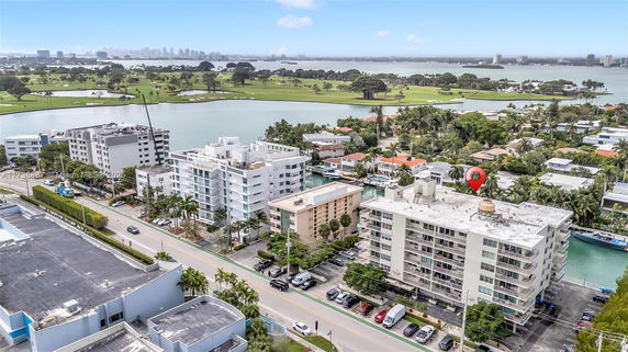 Aerial view of multi-story apartment buildings near water, with a golf course and city skyline in the background.