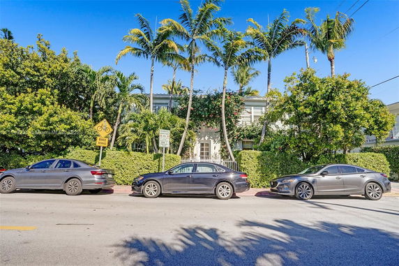 Front view of a two-story house with palm trees and parked cars.