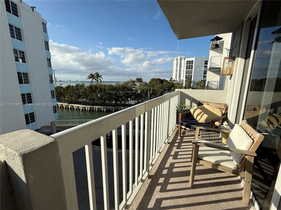 View from a balcony overlooking nearby buildings and a body of water surrounded by trees.