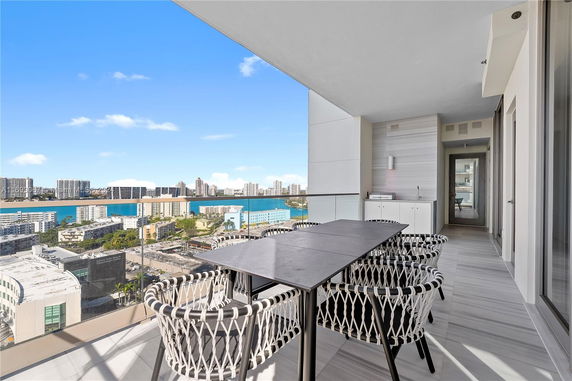 View from a modern balcony overlooking a cityscape with tall buildings and water in the background.