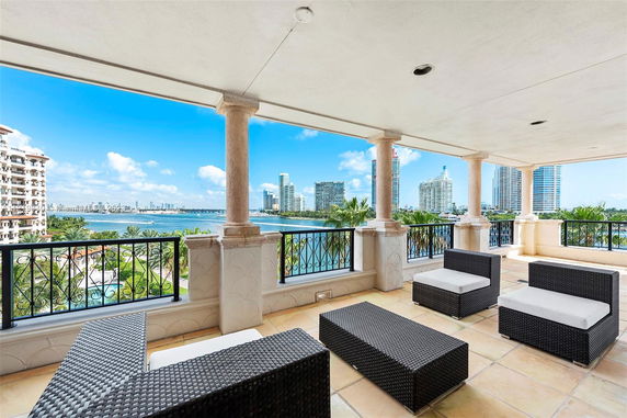 View from a covered balcony with outdoor seating overlooking a body of water and city skyline.