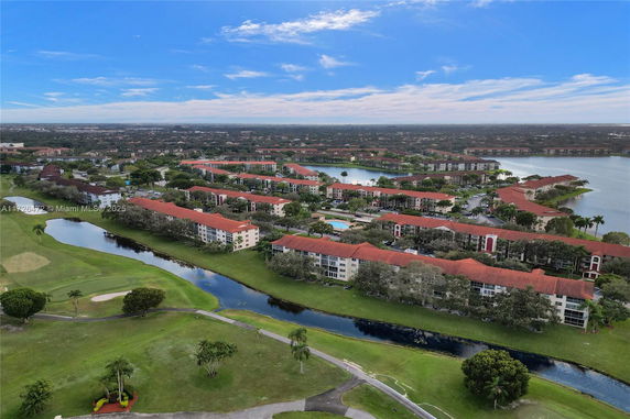 Aerial view of a residential complex with red-roofed buildings surrounded by greenery and water bodies.