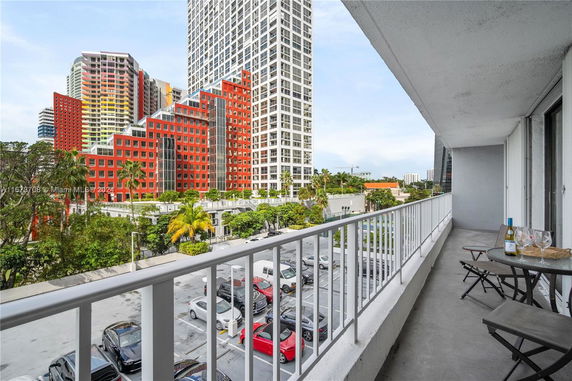 View from a balcony overlooking a parking area and colorful multi-story buildings.