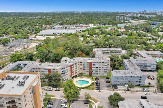 Aerial view of a residential complex with several buildings and a swimming pool, surrounded by greenery and urban infrastructure.