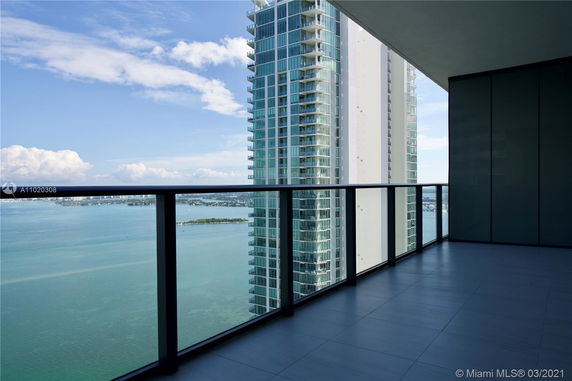 Balcony view from a high-rise building overlooking the sea and neighboring skyscraper.