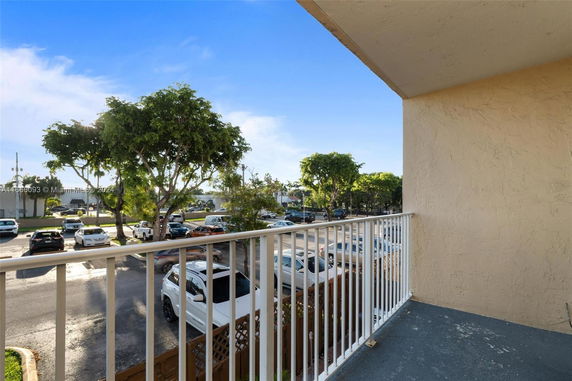 Balcony view overlooking a parking area with multiple cars and trees.