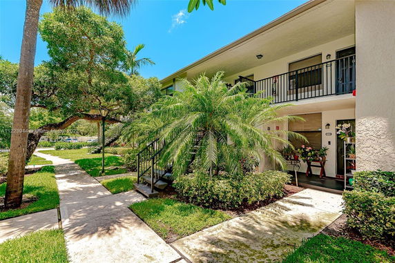 Front view of a two-story building with balconies and stairs surrounded by greenery.