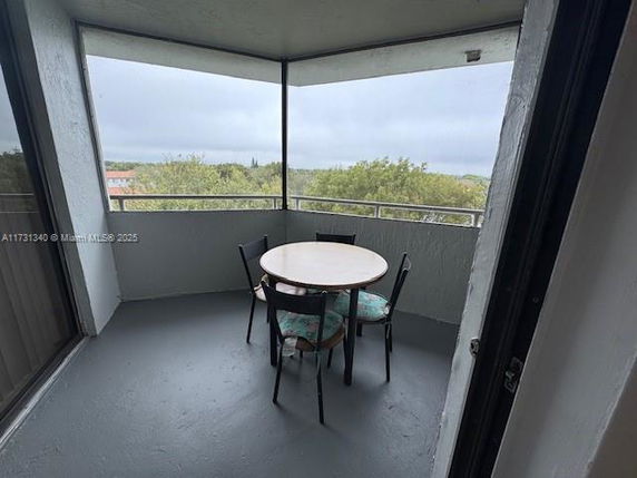 Outdoor balcony area with a round table and chairs, overlooking trees and distant surroundings.