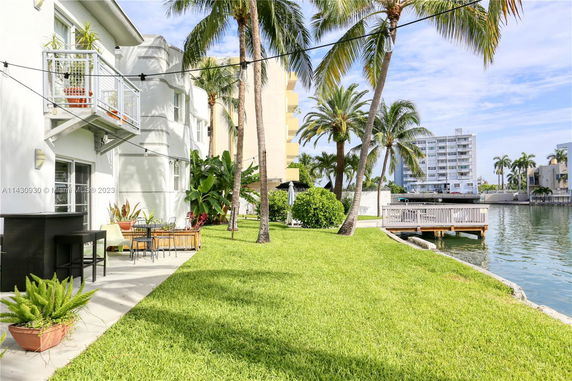 Backyard view of a building by a waterfront with a patio and palm trees.