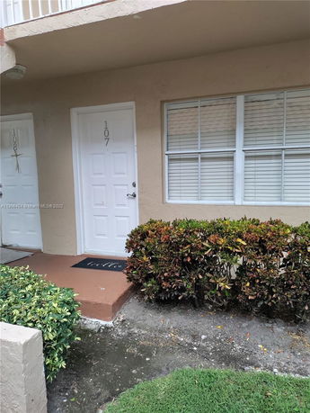 Front view of a building entrance with two white doors and bushes along the pathway.